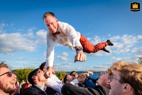 At Domaine des Plagnes, Saint-Hilaire-de-Brens, France, the groom is joyfully tossed into the air by cheering guests.